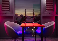 two chairs sitting at a table with microphones on it in front of a window