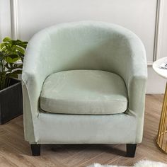 a light green chair sitting on top of a hard wood floor next to a potted plant