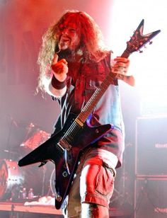 a man with long hair holding a black guitar in his right hand while standing on stage