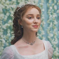 a woman wearing a tiara and dress in front of a floral wallpapered background