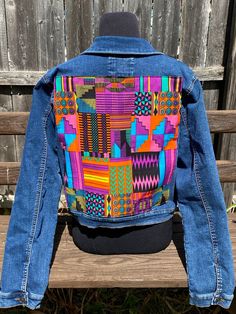 the back of a jacket with colorful designs on it sitting on top of a wooden bench