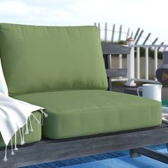 a green couch sitting on top of a wooden table next to a blue rug and coffee cup