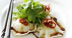 a white plate topped with dumplings covered in sauce and garnished with cilantro