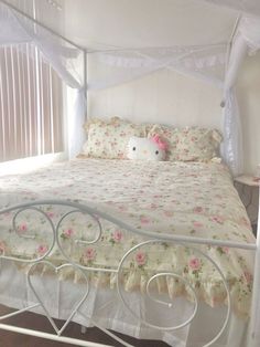 a white bed with pink flowers on it and a hello kitty stuffed animal in the corner