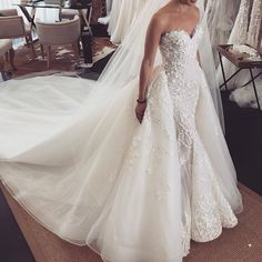 a woman standing in front of a mirror wearing a wedding dress with long train and veil