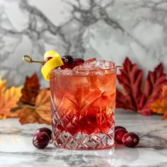 a glass filled with ice and cherries on top of a marble table next to leaves