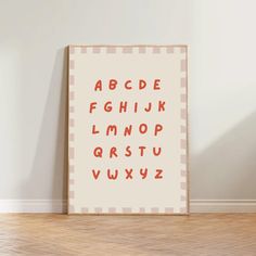 a poster with the alphabet on it in front of a white wall and wooden floor