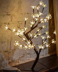 a lighted tree is sitting on a table in front of a brick wall and coffee cup