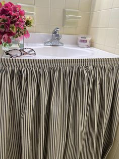 a bathroom sink with a striped skirt next to it and a vase filled with flowers