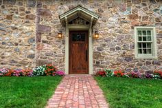 an old stone house with flowers in the front yard and brick walkway leading to it