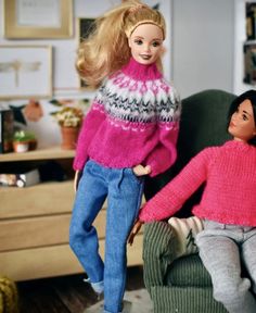 two dolls are sitting on a chair in the living room, one is wearing a pink sweater