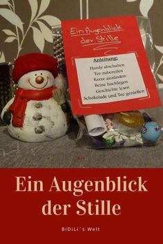 a small snowman with a red hat and scarf next to a sign that reads,'fin augenblick der stille '