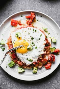 an egg is sitting on top of a plate with tomatoes, avocado and other toppings