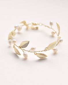 a gold bracelet with leaves and pearls on the side, sitting on a white surface