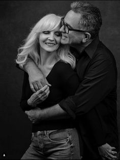 a man and woman embracing each other while posing for a black and white photo in front of a dark background