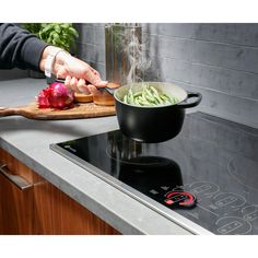 a person cooking vegetables on a stove top with a wooden cutting board next to it