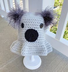 a crocheted koala hat is sitting on a white stand with grey hair