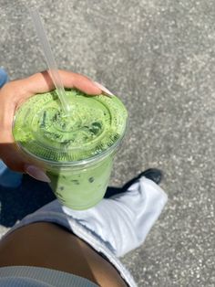 a person is holding a green drink in their left hand while standing on the pavement