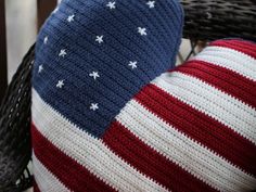 an american flag knitted pillow sitting on top of a wicker chair