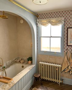 a bath tub sitting under a window next to a radiator in a bathroom