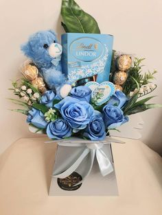 a blue teddy bear sitting on top of a box filled with flowers and chocolates