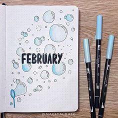 an open notebook with the word february written on it next to some markers and pens