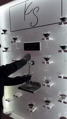 a man standing in front of a display of wine glasses on a wall with the name k s written on it