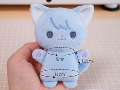 a hand holding a small blue stuffed animal with measurements for the cat's body