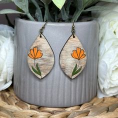 a pair of wooden earrings with flowers painted on them sitting next to a potted plant