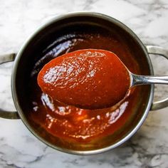 a spoon full of tomato sauce on top of a pot filled with red stuff and sitting on a marble countertop