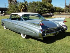 an old silver car parked on top of a lush green field