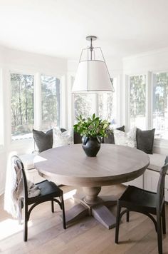 a dining room table with two chairs and a vase on top of it in front of some windows