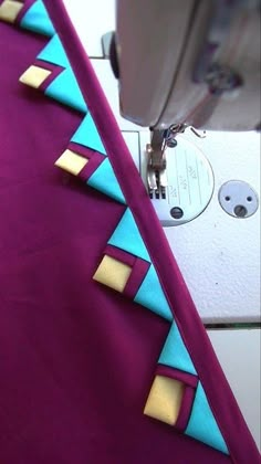 the sewing machine is working on the purple fabric with blue and gold trimmings