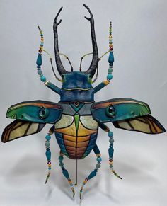 a blue and yellow bug with long antennae on it's back legs, surrounded by multicolored beads