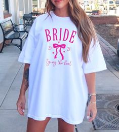 a woman wearing a white t - shirt that says bride, and has pink bows on it