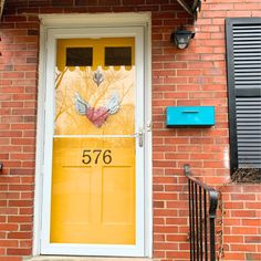 a yellow door with the number 756 painted on it in front of a brick building