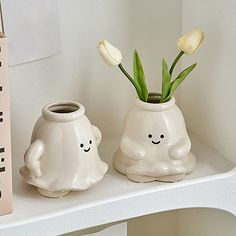 two white vases with flowers in them on a shelf