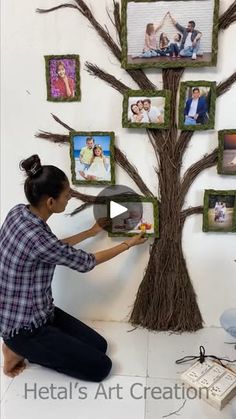 a woman sitting on the floor next to a tree with pictures hanging from it's branches