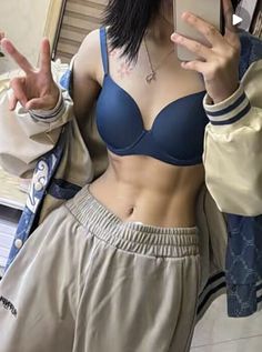 a woman in a blue bra top taking a selfie with her cell phone while wearing sweatpants