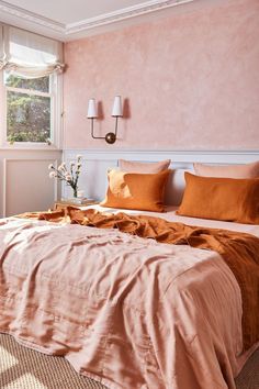 a bedroom with pink walls and orange bedding in front of a window that has two lamps on either side of the bed