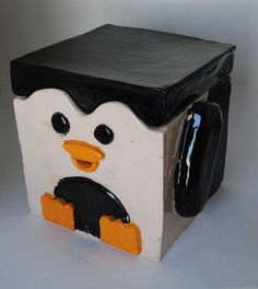 a ceramic penguin sitting on top of a white table next to a black and orange container