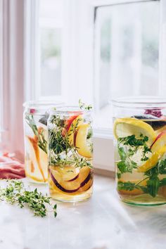 three jars filled with different types of vegetables and herbs sitting on a window sill