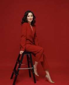 a woman in a red suit sitting on a stool