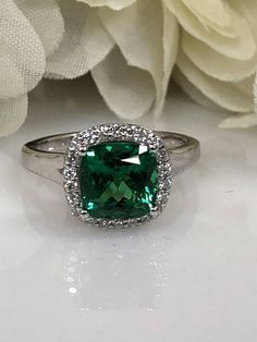 a ring with a green stone surrounded by white diamonds on a table next to flowers