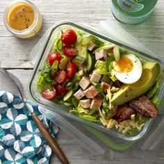 a salad with bacon, avocado, tomatoes and an egg in it on a wooden table