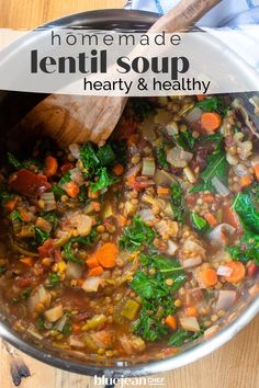 a pot filled with lentil soup and vegetables on top of a wooden table next to a spoon