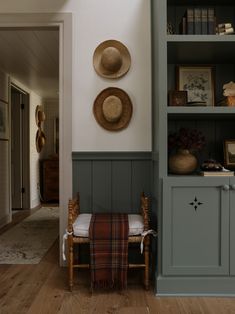 two hats are hanging on the wall next to a chair and bookshelf in a room