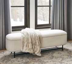 a white bench sitting in front of two windows covered with blankets and fur on top of it