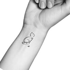 a black and white photo of a hand holding a cat tattoo on it's wrist