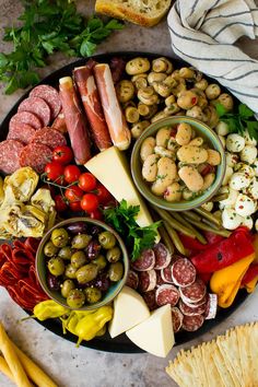 a platter filled with meats, cheese and olives next to bread sticks